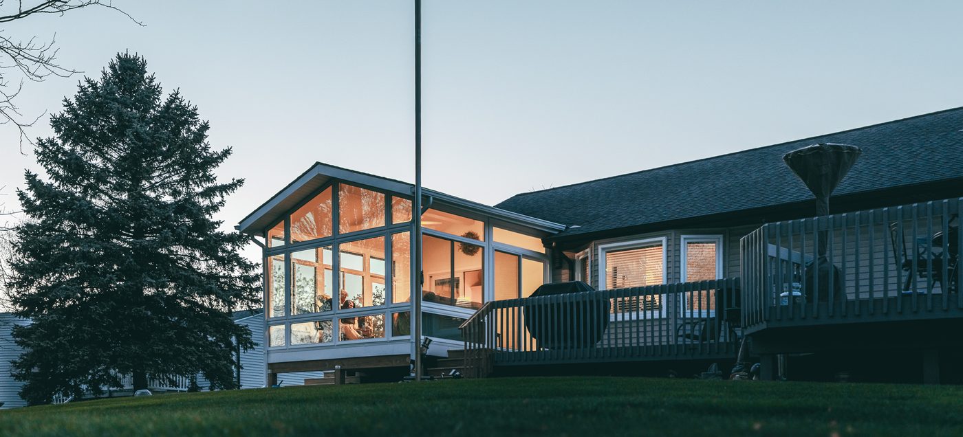 Four-season LivingSpace sunroom addition glowing at dusk on a South Jersey home, American flag by the entry