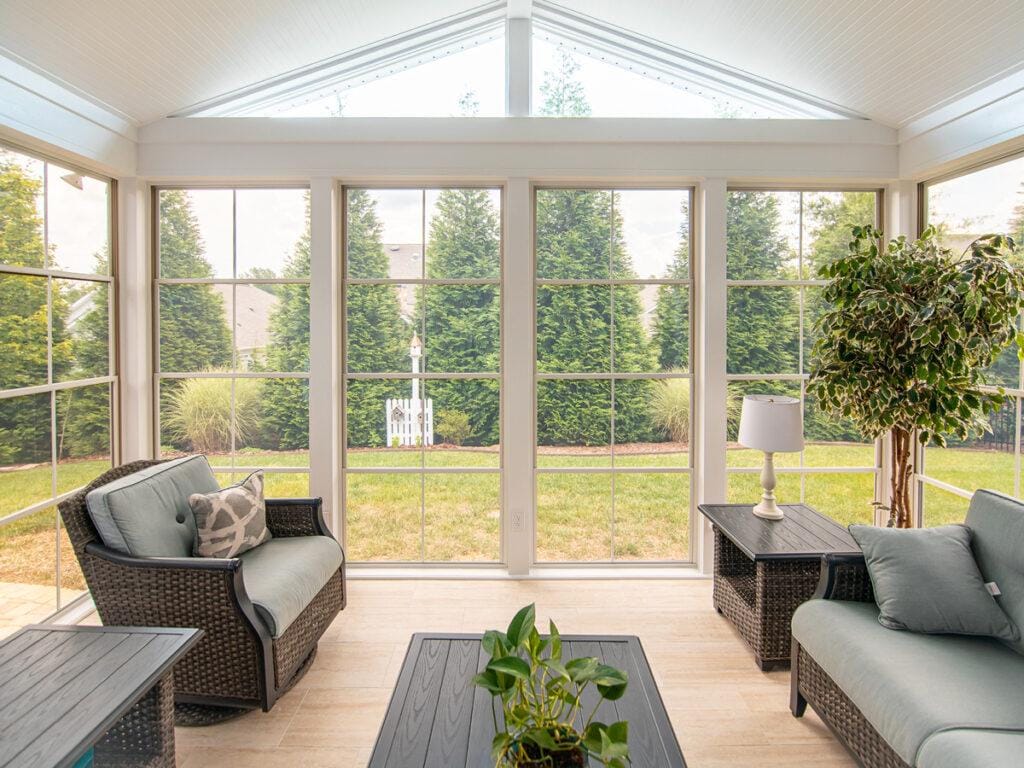 Three-season room interior with white-framed glass walls and wicker furniture overlooking a South Jersey backyard